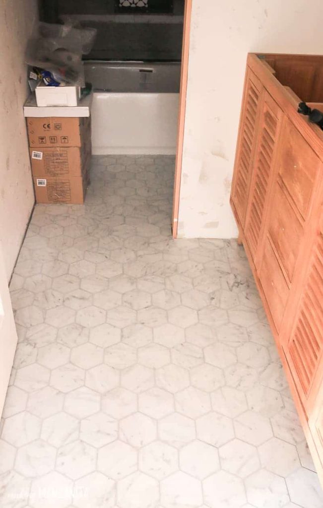 Marble hexagon tile floors in bathroom under renovation with gray grout and wood vanity