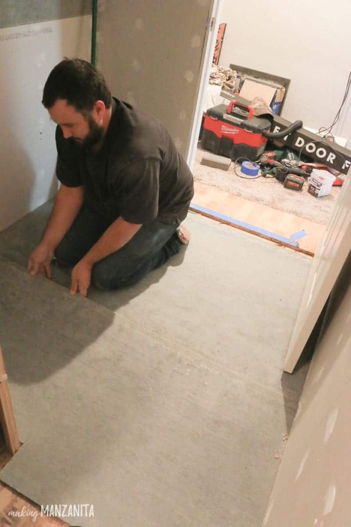 Man laying sheet of concrete backer board on floor before starting to tile the floor