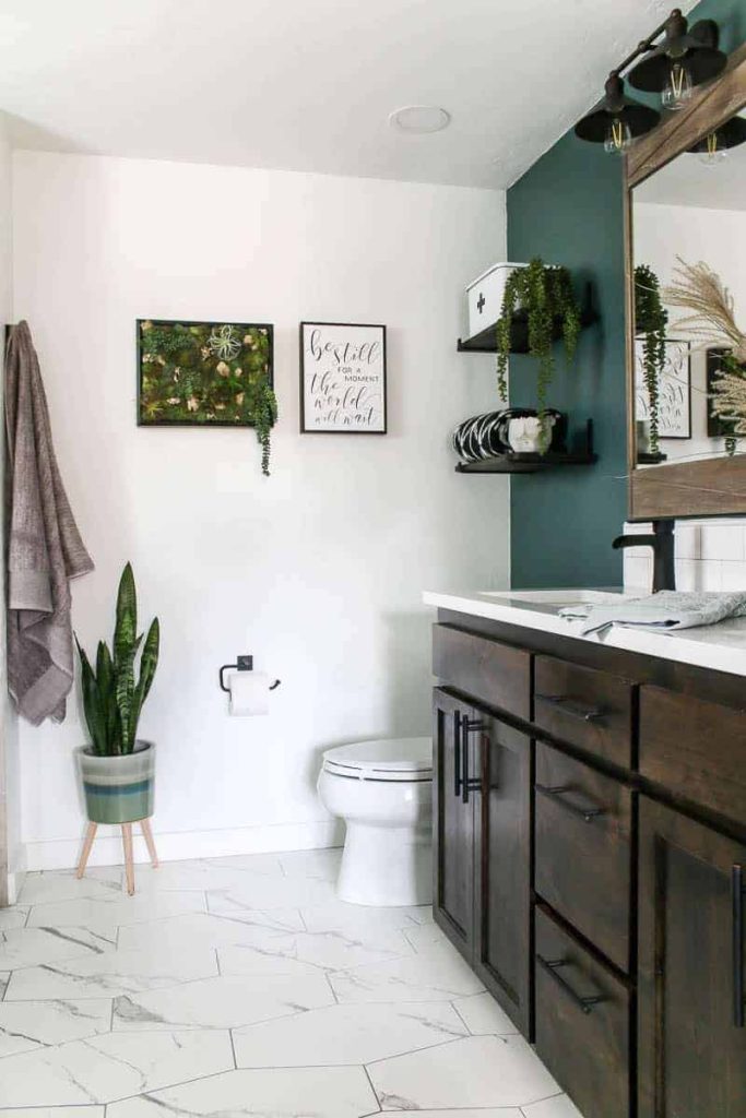 Modern bathroom with marble hexagon tiles on the floor and a dark wood vanity with green accent wall with floating shelves above a toilet 