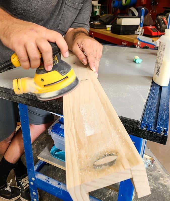 A man is sanding wood in preparation for a picture ledge.