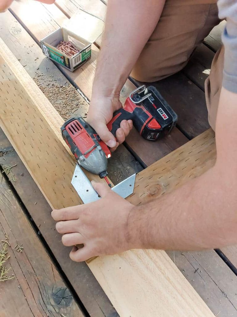 Man attaching two boards for frame on a gate and corner brackets with deck screws using drill