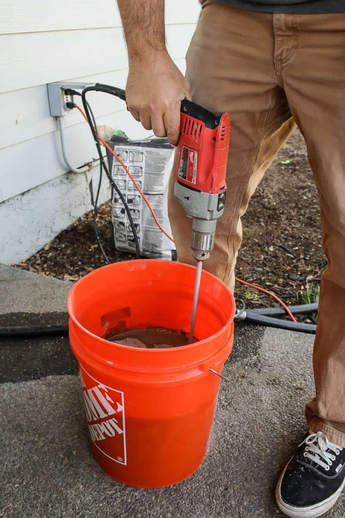 Man holding the drill to mix the thinset and water inside bucket before installing tile