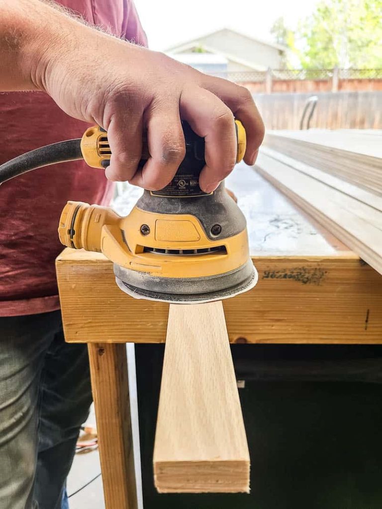 Man holding orbital sander sanding wood slat