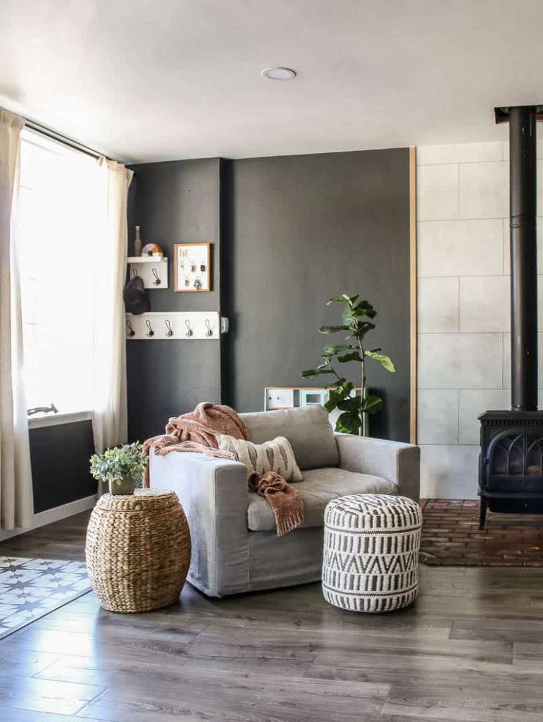 After image of comfy light grey armchair for Article furniture Alzey in Whistle gray beside the wood stove with patterned boho pouf as a footrest on a modern boho living room.